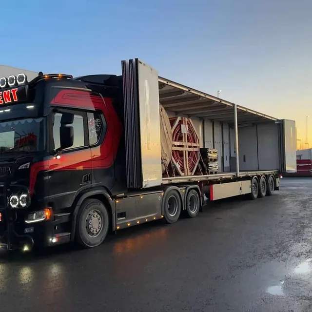 Svart og rød lastebil med åpen henger i solnedgang.