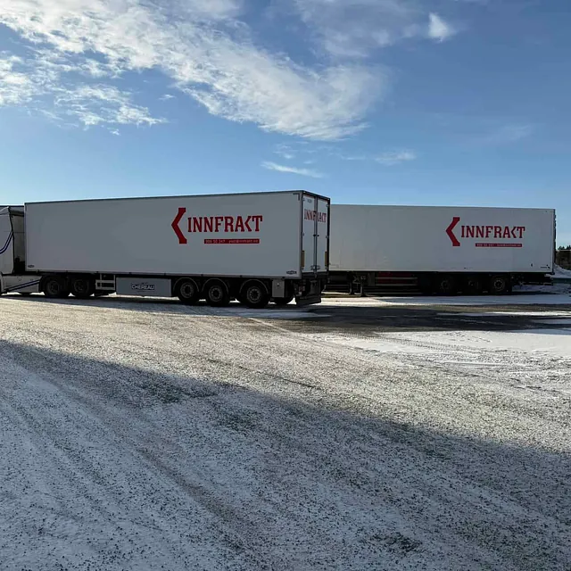 To hvite lastebiler parkert på snødekt plass.