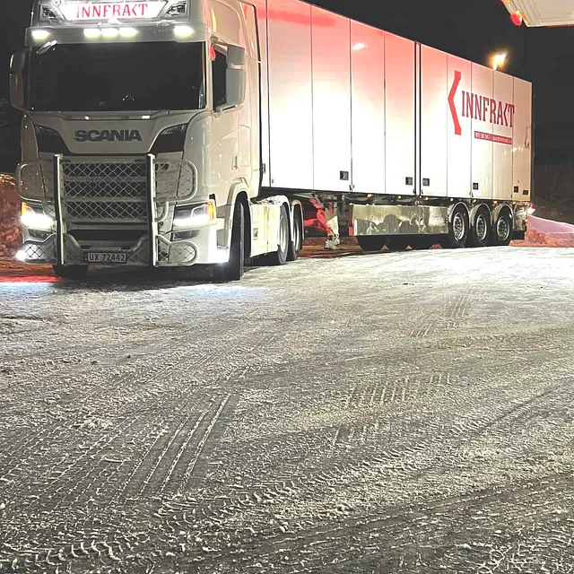 Hvit lastebil parkert ved en bensinstasjon om natten.