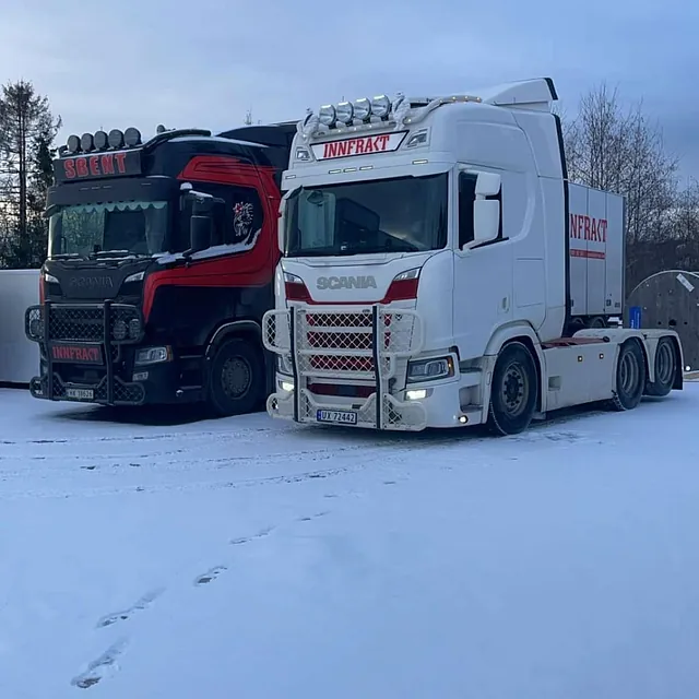 Hvit og svart lastebil parkert på snødekt vei.