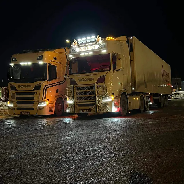 To hvite lastebiler parkert på en mørk vei.