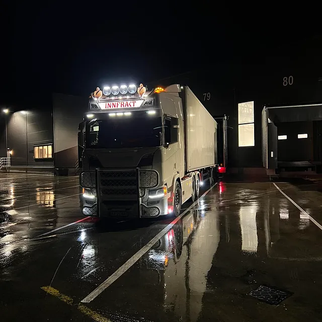 Hvit lastebil parkert ved lagerbygg om natten.